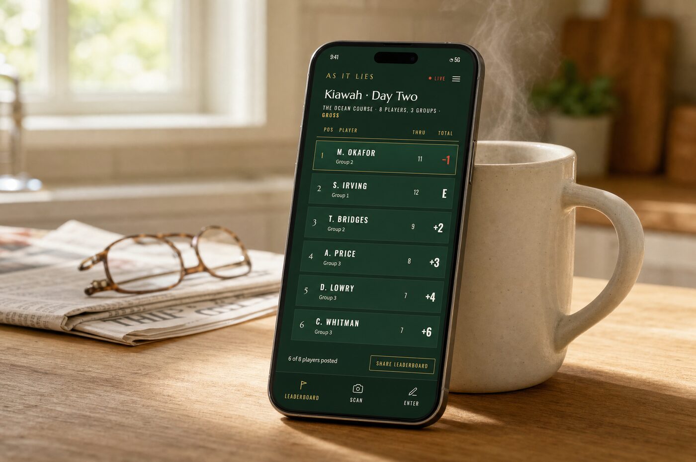 A phone propped against a coffee mug on a kitchen counter, showing the live leaderboard