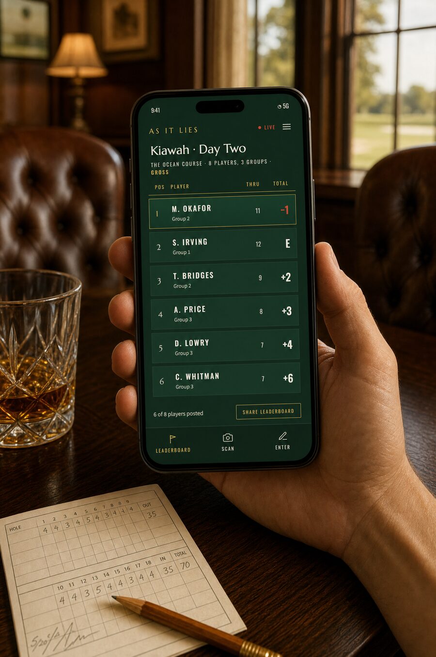 The live leaderboard held in hand in the clubhouse, whiskey and the paper scorecard on the table