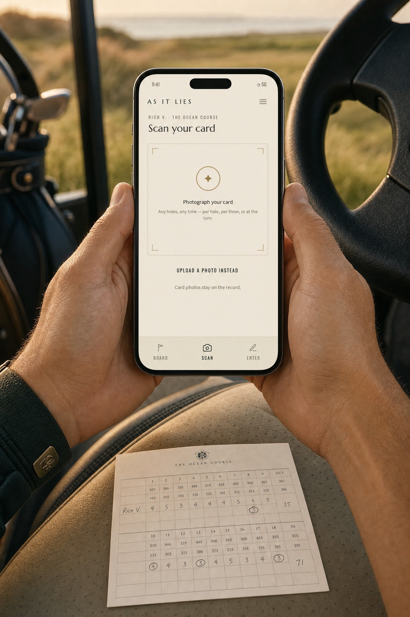 A golfer in a cart holding a phone open to the Scan screen, a paper scorecard on the seat